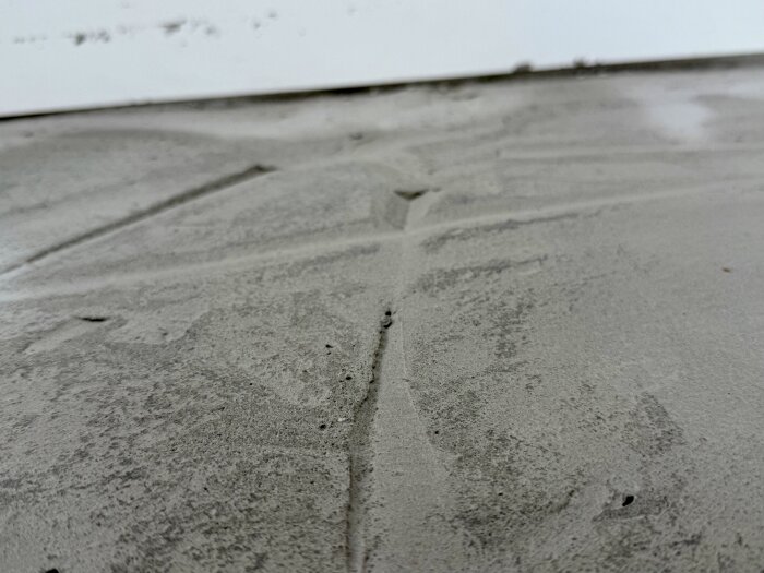 Betonggolv med ojämnheter och synliga hål, troligen från misslyckad flytspackling, i ett uterum.