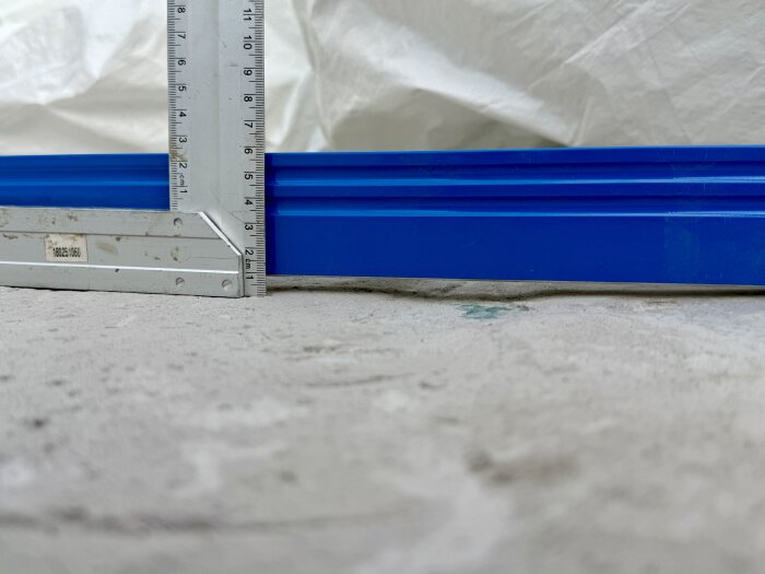 Bilden visar ett flytspacklat golv med en blå nivålist och linjal som mäter djupet på ojämnheter.