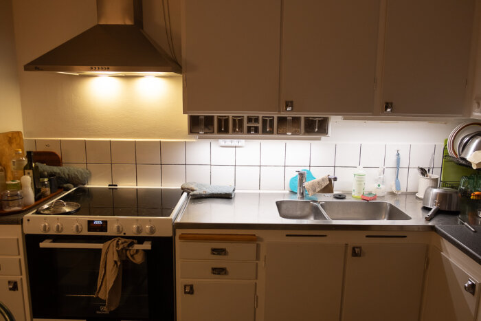 Ett kök med spis, diskbänk och diskho, omgiven av olika hushållsföremål och diskmedel.