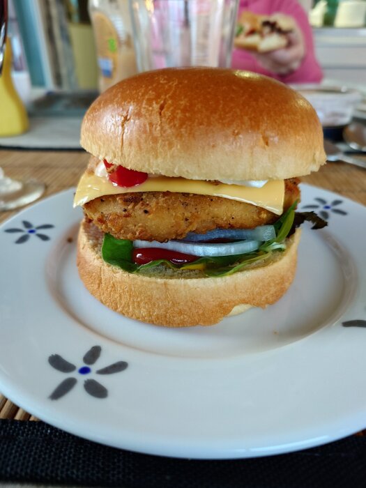 Kycklingburgare med ost, sallad, rostad och silverlök på en vit tallrik, toppad med inlagd chili och krämig dressing.