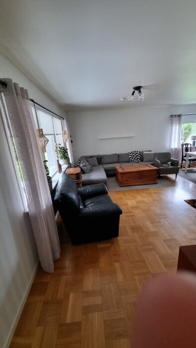 Vardagsrum med hörnsoffa, soffbord och fåtölj. Fingret skymmer del av bilden.