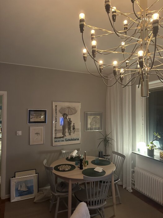 Matbord med gröna bordstabletter, omgiven av stolar och tavlor på väggen. Inget synligt belysningsmonterat över bordet i rummet.