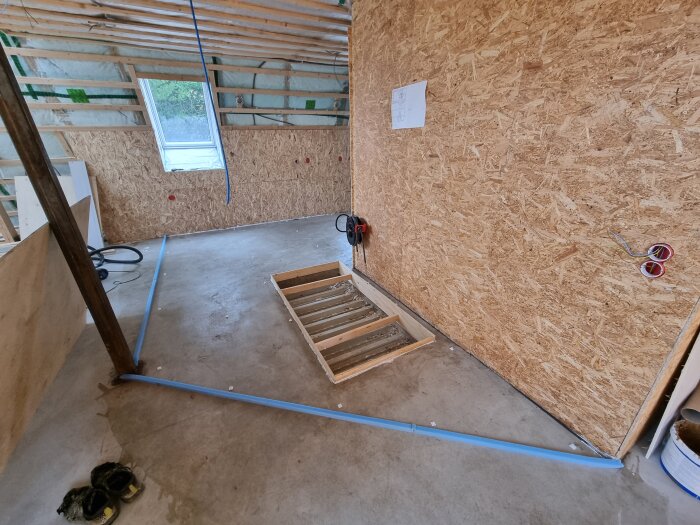 Nyspacklat golv i rum under renovering med träväggar och synliga bjälkar.