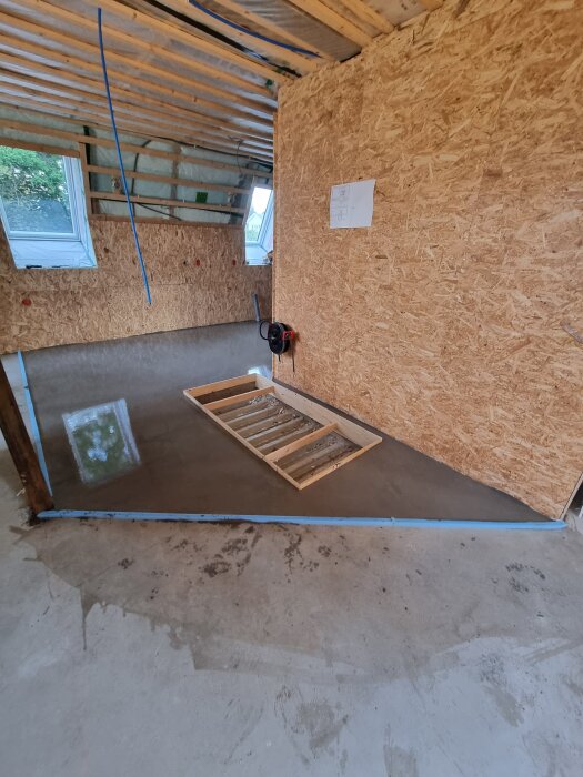 Nyspacklat golv i ett rum under renovering med träväggar och takbjälkar.