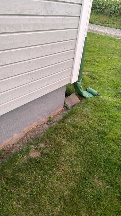 Stuprörsidyll med grönt provisoriskt fäste vid en villa, omgiven av gräs och del av grundmurens hörn synligt.