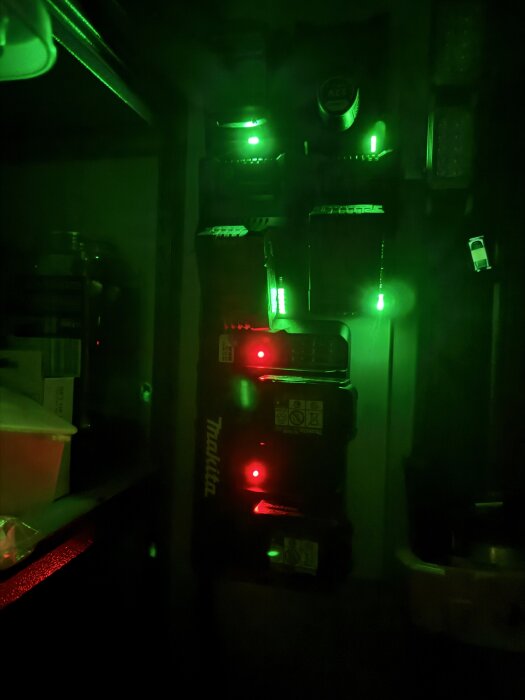 Batteriladdare med lysande gröna och röda lampor i ett mörkt rum.