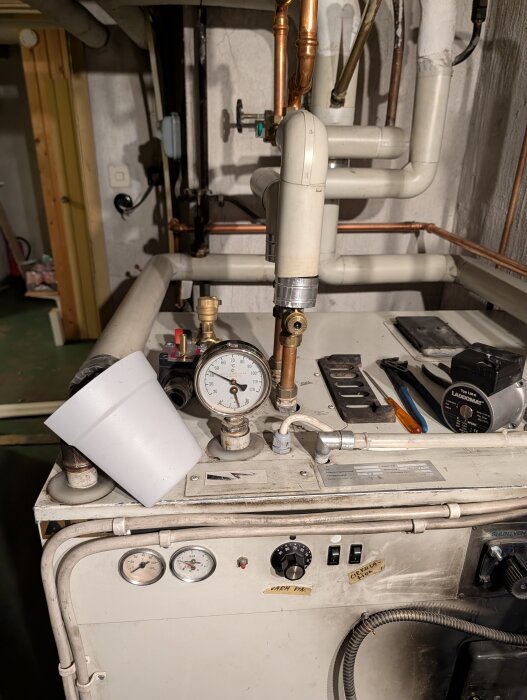 Uppvärmningssystem med tryckmätare och rör i ett pannrum. Vredet på systemet är trasigt, vilket orsakar läckage när det vrids.