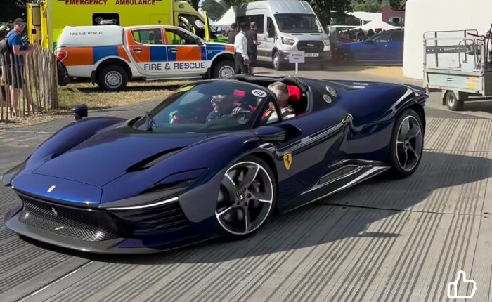 Blå sportbil med elegant design på evenemang, ambulans i bakgrunden.