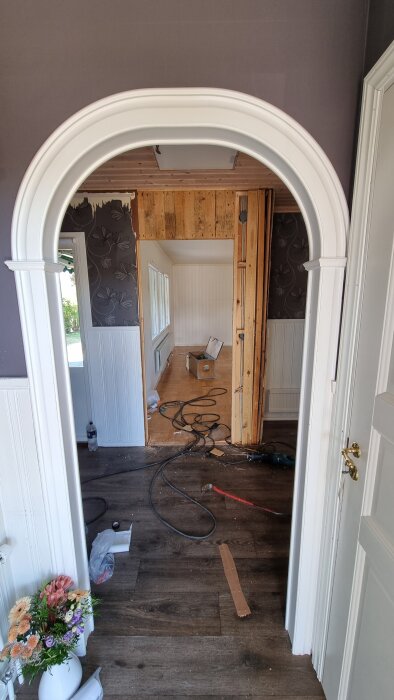 Renoveringsprojekt med en rivet valvöppning i ett rum. Sladdar på golvet, en papperskorg och en blomvas syns i förgrunden.