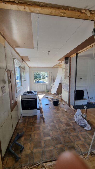 Rivningsprojekt i kök med borttagen vägg, exponerade rör och golv. En spis står kvar och material ligger spritt på golvet.