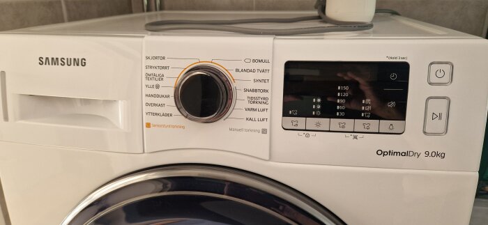 Närbild av en Samsung torktumlare med ratten inställd på olika torkprogram och en släckt display.
