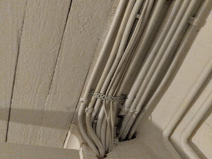 Elledningar i en trång installation med flera vita kablar som är bundna ihop på en vägg.