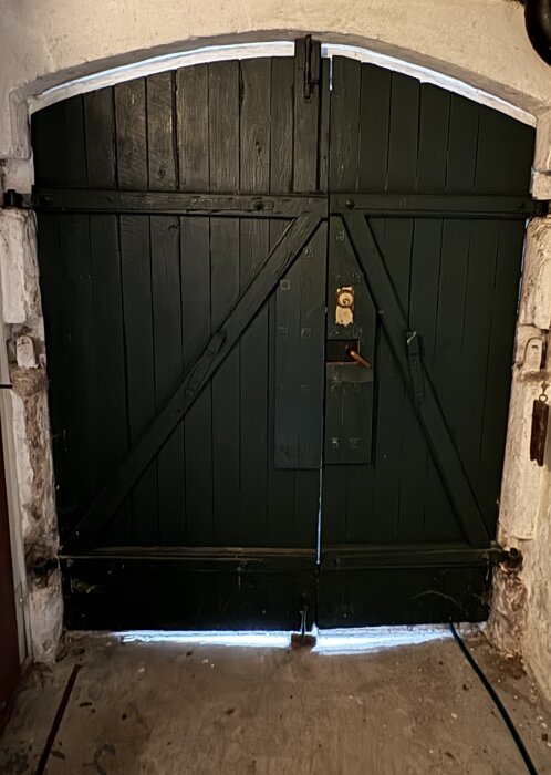 Slagport med glipor i ovankant och nederkant, ljus syns igenom. Porten är mörkbrun och monterad i en vit vägg.