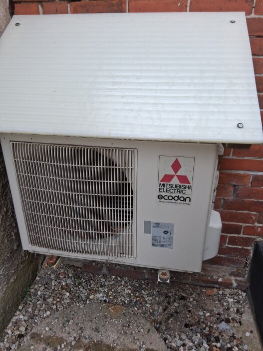 Utomhusenhet för Mitsubishi luftvärmepump mot tegelvägg, del av system för att sänka kostnader vintertid.