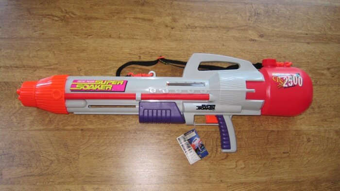 Super Soaker CPS 2500 vattenpistol på ett trägolv, med färgerna röd, grå och lila, en ikonisk leksak för vattenkrig från 90-talet.