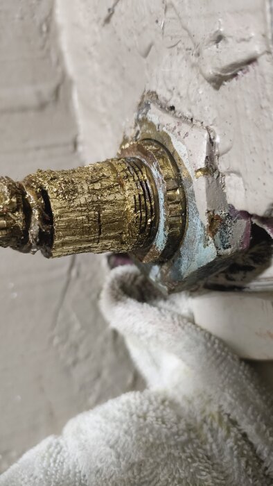 Trasigt slottsvred med synligt slitage och tecken på rost, sitter mot en vägg med handduk delvis synlig under vredet.