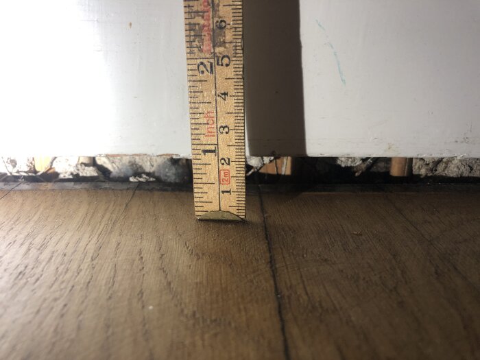 Linjal mäter glipa mellan golv och vägg i bostadsrätt, antydande sättning eller strukturellt problem.