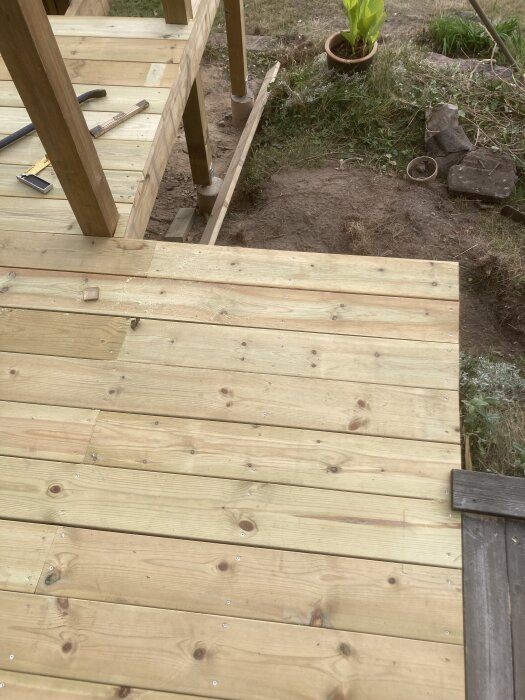 Altanen i trä med måttband och hammare, visar olika vinklar i ett snickeriprojekt. Bakgrunden har jord och en kruka med växt.