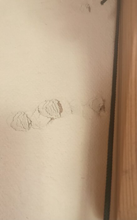 Förstorad bild av väggen med struktur och sprickor nära en träkant.