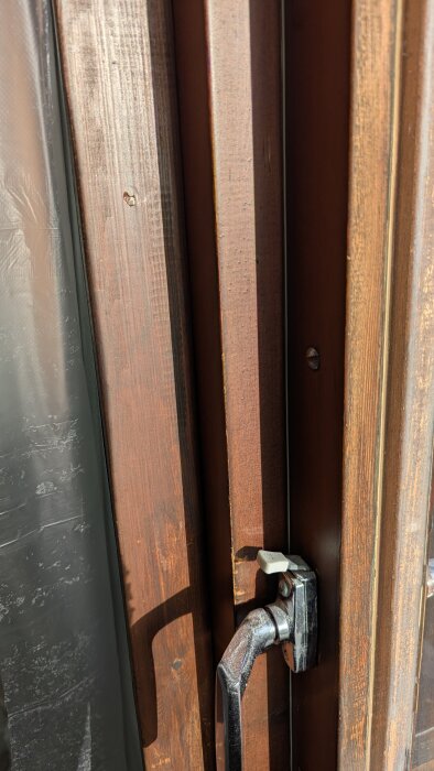 Närbild av brun träaltandörr med metallhandtag, visar slitage på träytan.