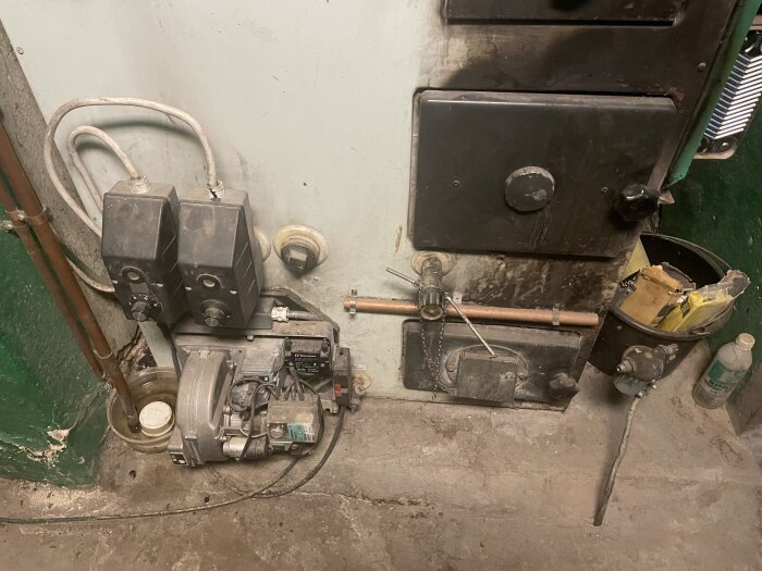 Äldre kombinationspanna med synliga rör och ventiler, smutsig yta och verktyg i närheten.