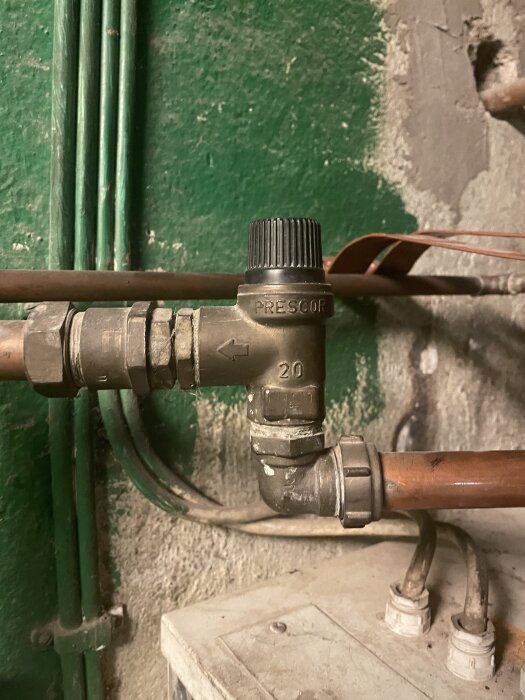 Ventil med tryckreglering på kombinationspanna, märkt "Prescor", ansluten till kopparrör framför grön vägg och grå sten.