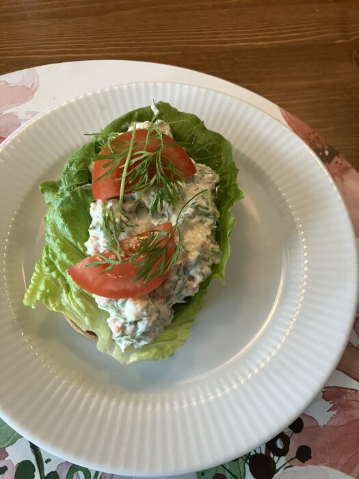 Toast med kräftstjärtar på salladsblad, toppad med tomatskivor och dill på en vit tallrik.