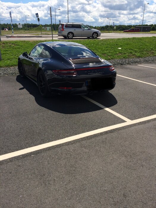 Svart bil parkerad över två parkeringsrutor på en parkering.