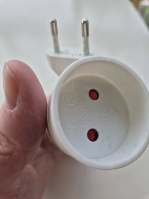Närbild på en hand som håller en S-märkt ojordad stickkontakt och adapter för nätström.
