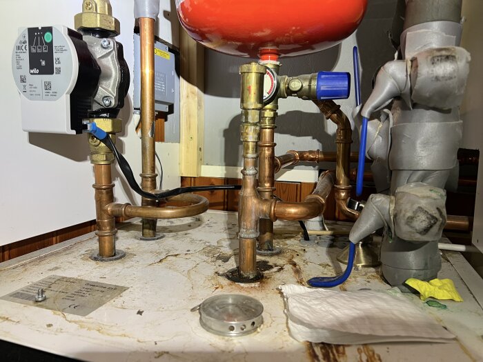 Expansionskärl med rör och ventiler vid bergvärmepump, visar manometer på noll tryck samt rör för övertrycksventil och anslutna kopparrör.