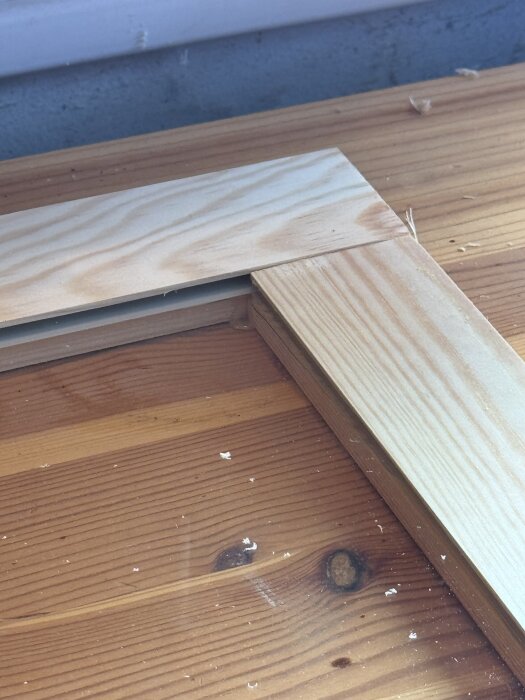 Hörnet av en träram med planhyvlat furu ligger på ett arbetsbord, del av ett DIY-projekt för en garderobsinredning med glashyllor.