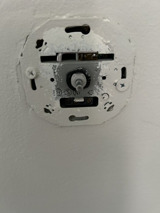 Övermålad dimmer installerad i en vägg, monteringsskruvar synliga.