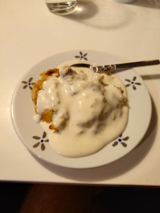 Tallrik med äppelpaj och vaniljsås på ett vitt bord.