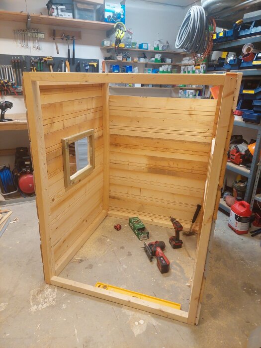 Byggkonstruktion av trä med väggar och fönsteröppning, verktyg på golvet i garageverkstad.