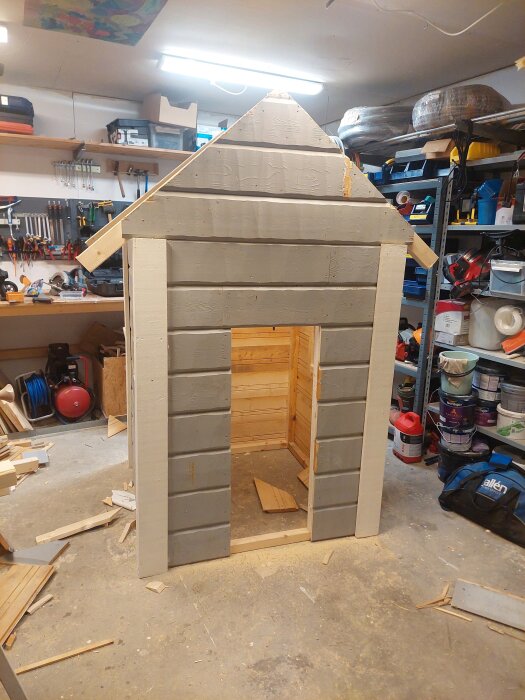 Lekstuga under konstruktion i ett garage, byggd av rivnings- och spillvirke, med avtagbart tak och gavel för enkel transport.