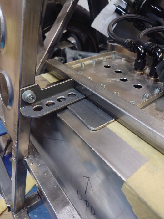 Fäste för bränsletank och början på golvet i ett bagageutrymme, tillverkat i metall med flera monteringshål och synliga skruvar.