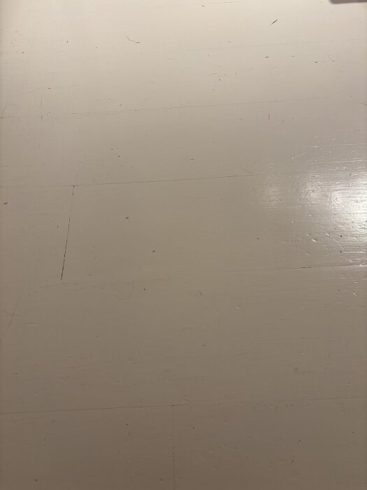 Målat furuparkettgolv med slitage och repor synliga på ytan, innan renovering till ursprungligt trägolv.