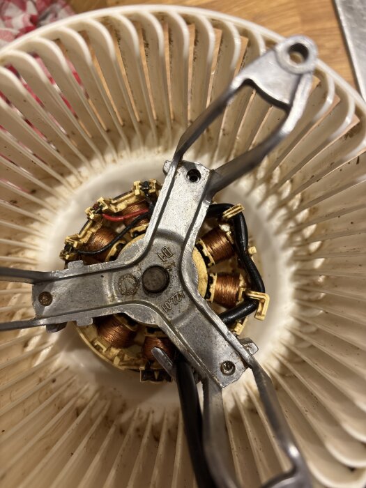 En motor med exponerade koppartrådar och metallkomponenter, sett uppifrån inuti en vit plastkonstruktion.