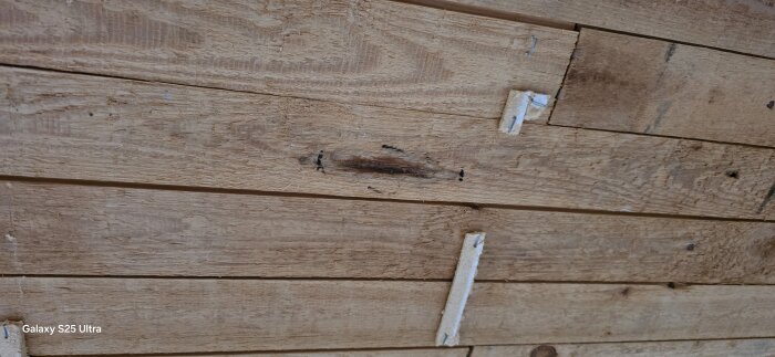 Närbild av träpanel med synliga mörka fläckar och skruvhål, relaterat till en rapporterad vattenskada i ett äldre hus.