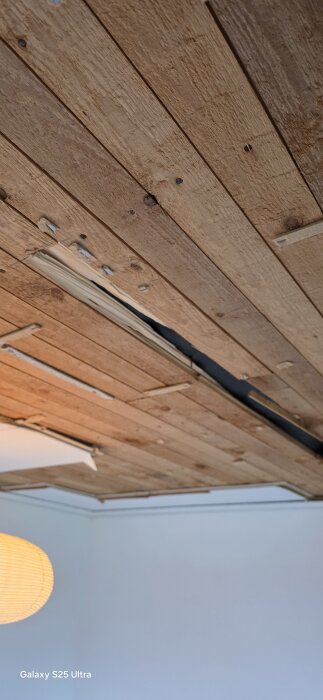 Tak med öppnad panel som visar fuktskada och blottad råspont, med en lampskärm synlig i nedre vänstra hörnet.