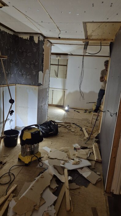 Renoveringsprojekt med delvis rivna väggar, lösa kablar och byggmaterial utspritt på golvet i en framtida matsal och hall.