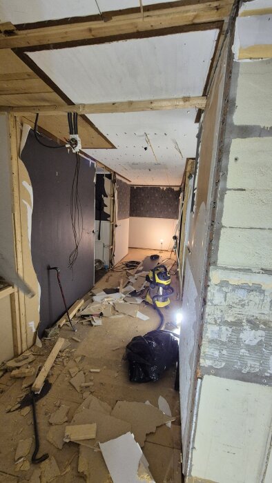 Renoveringsarbete med utriven parkett och tak, skräp på golvet, verktyg och belysning synliga i ett rum under ombyggnad.