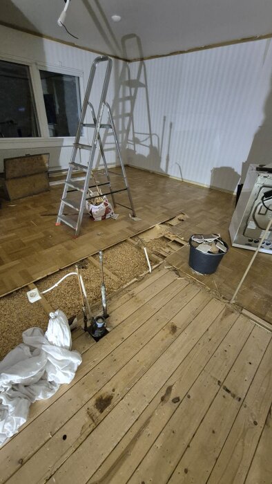 Rum under renovering med stege, rivet parkettgolv och synliga rör. Verktyg och byggmaterial syns i bakgrunden.