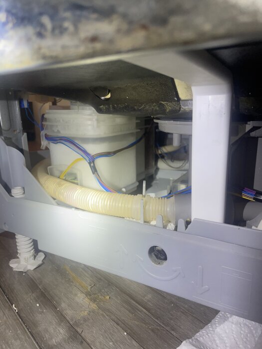 Diskmaskinens insida med avloppsrör, kablar och delvis igensatta delar synliga; rengjordes och monterades om.