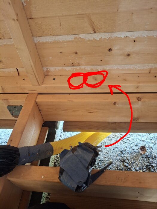 Bygget av en friggebod med isolering, två markerade områden på träregel för elektriska installationer, gul slang och marken synlig under.