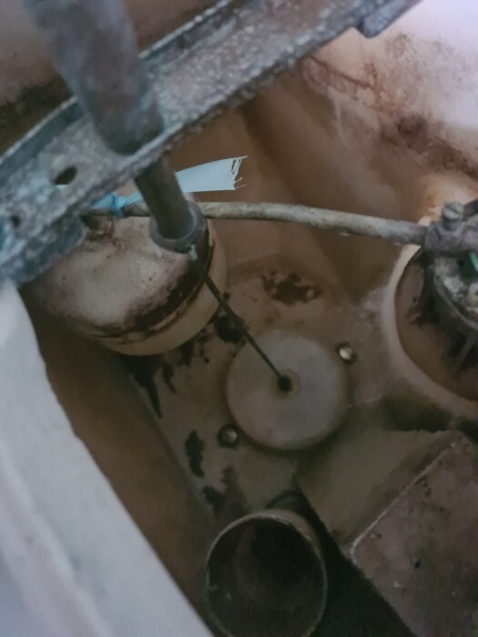 Toastolens cistern med en gammal, krackelerad tätning vid botten, synlig med rör och mekanismer omkring.