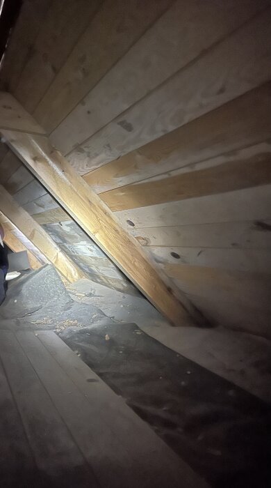 Vind med träpanel och isolering samt synliga spånrester på golvet; inspekteras för mögel och röta.
