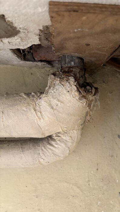 Slitet rör med skadad isolering och fibermaterial i källare, potentiellt problem för hantering och renovering.