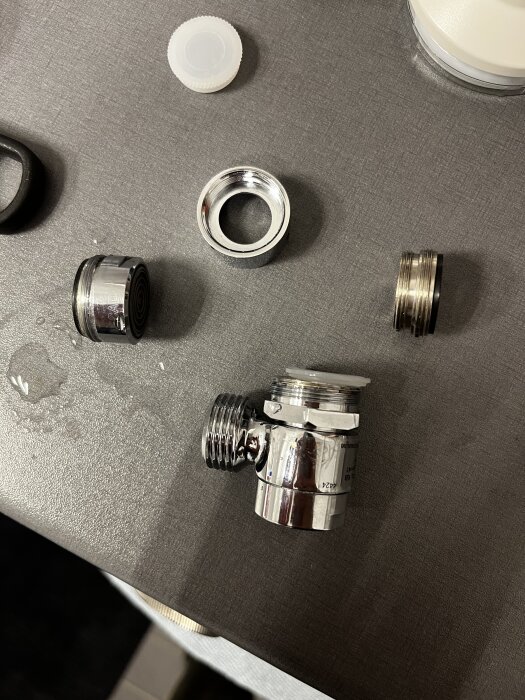 Olika delar för handduschmontering, inklusive en tvättblandare med omskiftare, strålsamlare och adapters på en bänkskiva.