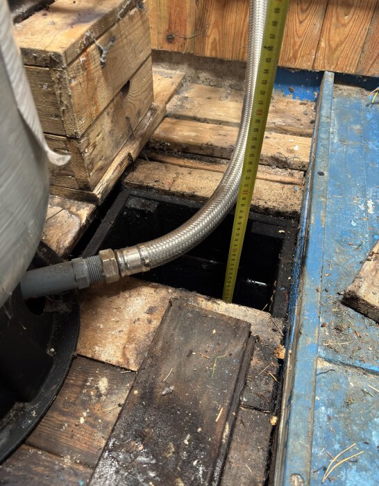 Brunn i källare med träomgivning, vattenpump, trälåda och måttband synliga, diskuteras service och vattenkvalitet.